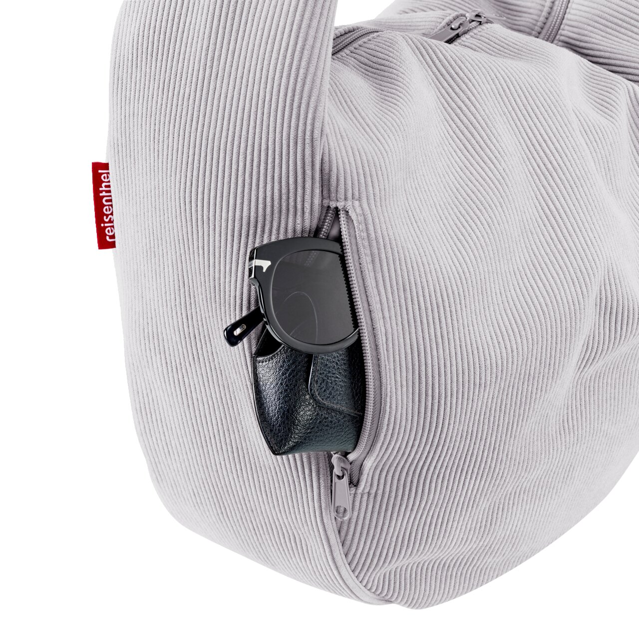 Hellgraue Reisenthel Cord-Tasche mit Reißverschluss-Seitenfach, darin Sonnenbrille und kleines Etui; Detailansicht von der Seite in leichter Schrägansicht