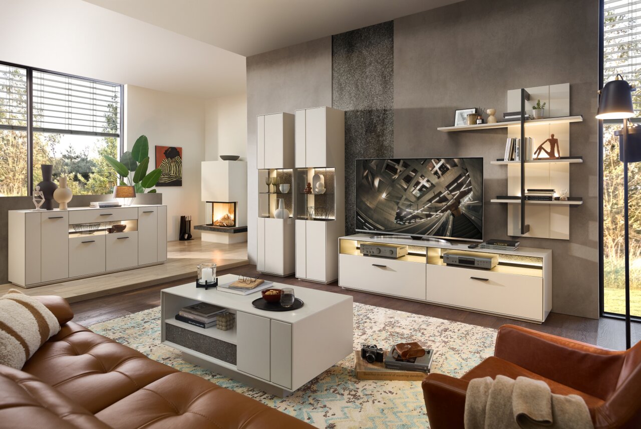 Moderne Wohnzimmer-Wandkombination in heller Farbe mit TV-Schrank, Regalen und Vitrinen, seitliche Perspektive.
