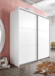 Moderner weißer Schwebetürenschrank mit zwei Türen, seitliche Perspektive, vor einer gemusterten Wand und auf einem Holzboden stehend.