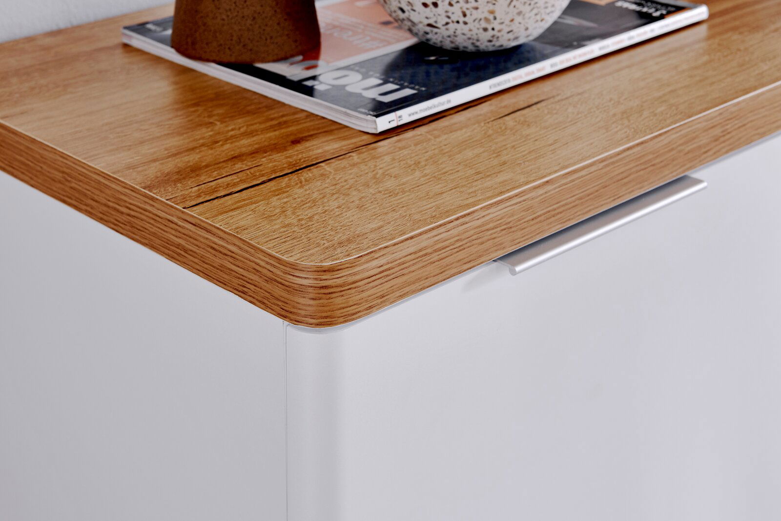 Nahaufnahme eines Sideboards mit einer Holzoberfläche und einer weißen Front, von oben betrachtet.