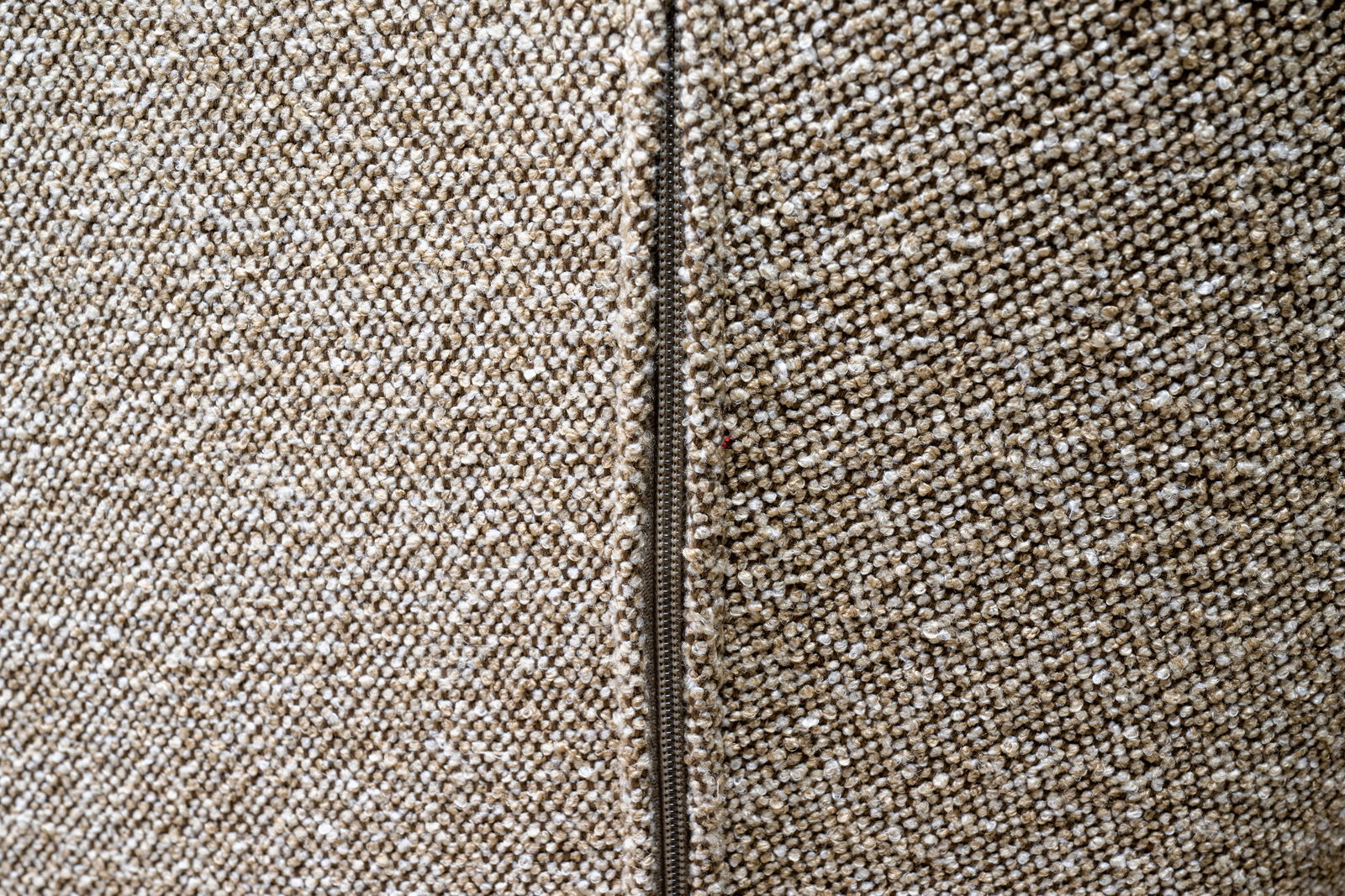 Nahaufnahme eines beigen Stoffes mit Reißverschluss, perspektivisch von der Seite aufgenommen.