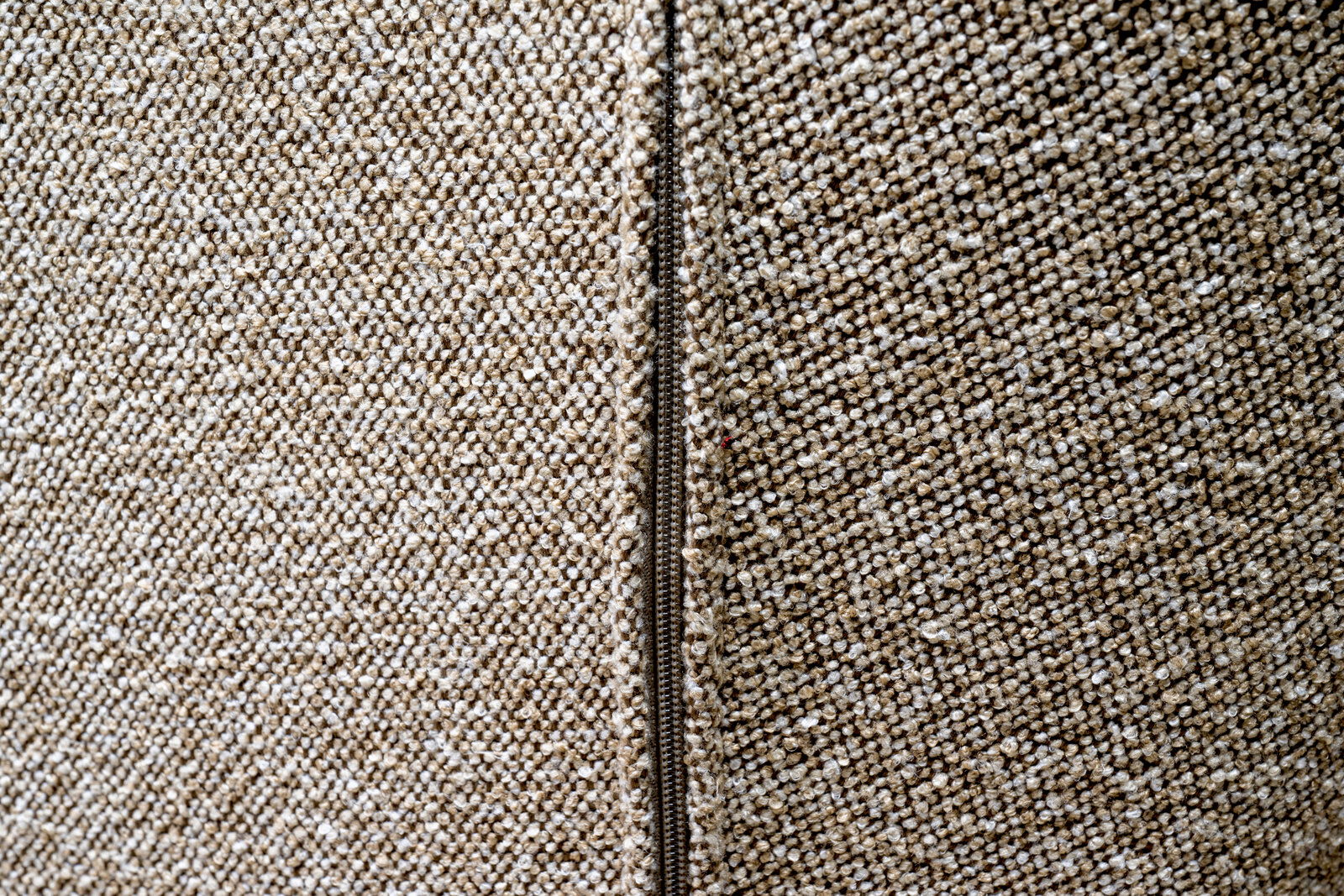 Nahaufnahme eines beigen Stoffes mit Reißverschluss, perspektivisch von der Seite aufgenommen.