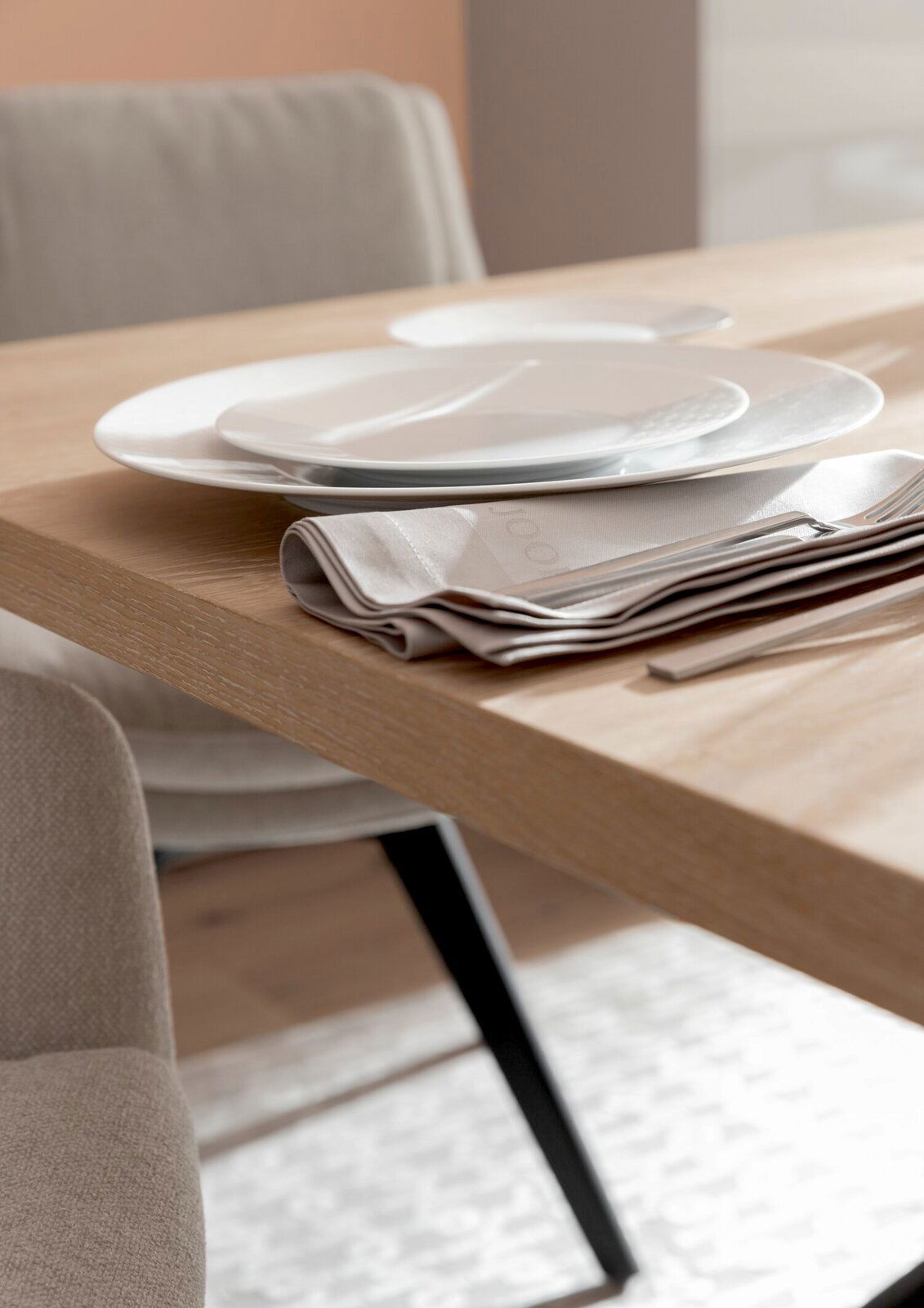 Nahaufnahme eines gedeckten Esstisches mit Holzoberfläche, weißen Tellern und beigen Stoffservietten, seitliche Perspektive