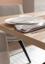 Nahaufnahme eines gedeckten Esstisches mit Holzoberfläche, weißen Tellern und beigen Stoffservietten, seitliche Perspektive