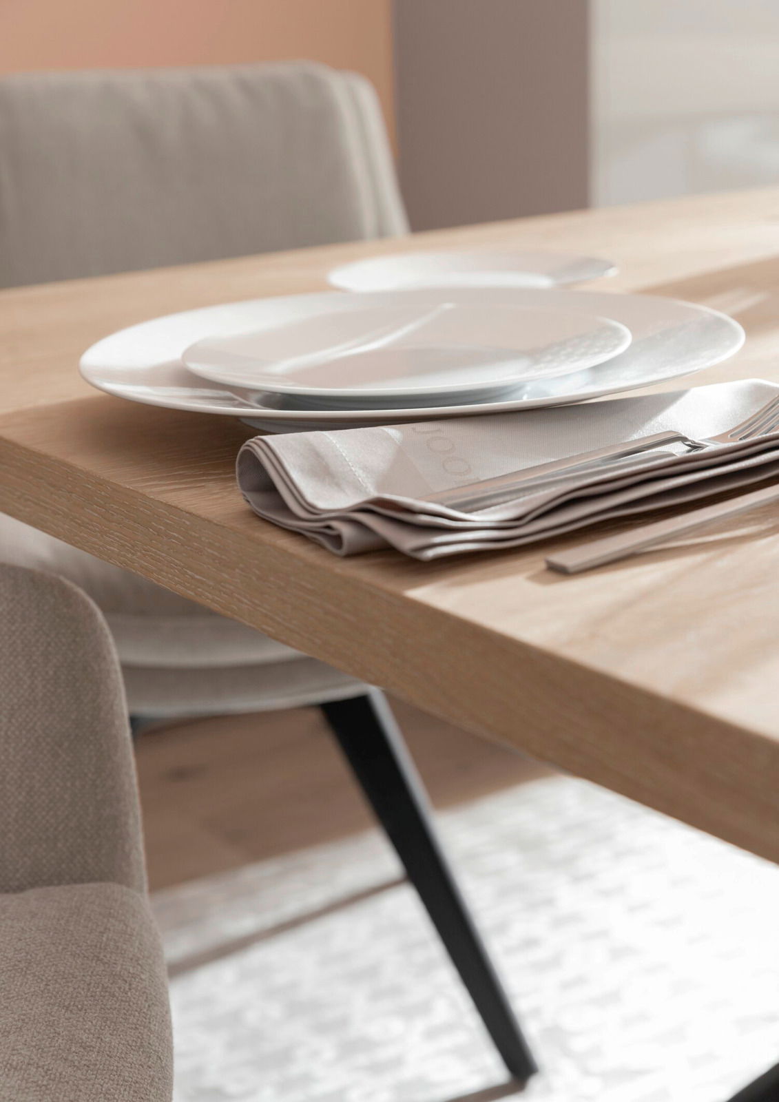 Nahaufnahme eines gedeckten Esstisches mit Holzoberfläche, weißen Tellern und beigen Stoffservietten, seitliche Perspektive