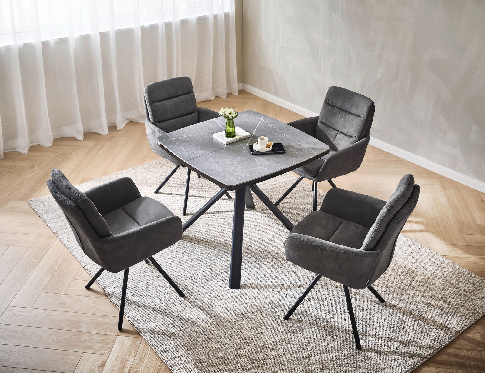 Vier graue Armlehnstühle um einen quadratischen Tisch in einem modernen Esszimmer, aus der Vogelperspektive fotografiert.