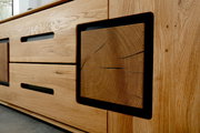 Detailaufnahme eines modernen Sideboards aus hellem Eichenholz mit sichtbarer Maserung, schwarzen Griffaussparungen und dekorativem Stirnholz-Element im schwarzen Rahmen, fotografiert aus schräger Frontperspektive