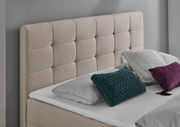 Beige gepolstertes Boxbett mit gestepptem Kopfteil, dekoriert mit Kissen in verschiedenen Farben, seitliche Perspektive.