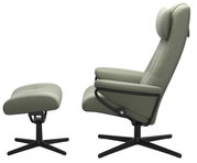 Zijaanzicht van een groene fauteuil met bijpassende voetenbank, beide met een zwart draaipootje.