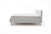 Zijaanzicht van een modern gestoffeerd bed in lichtgrijs met houten poten en een gestoffeerd hoofdeinde.