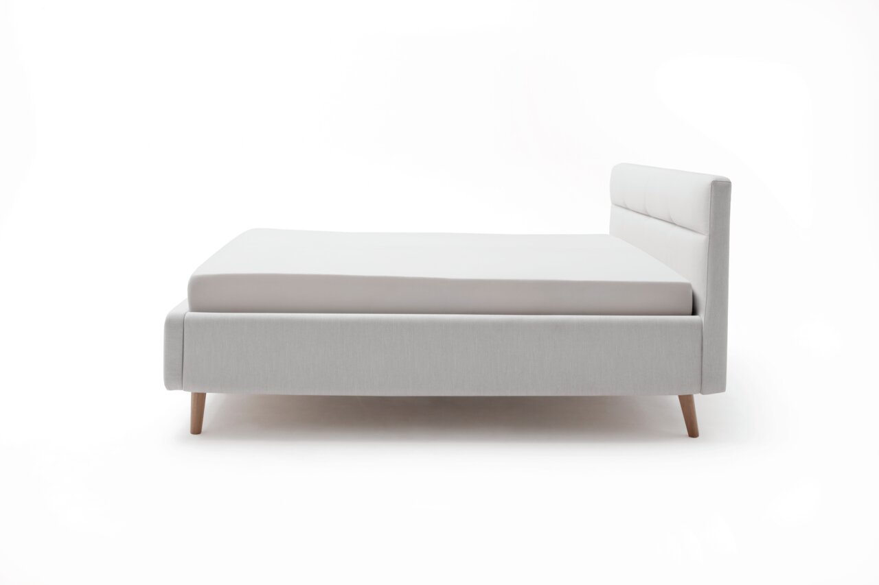 Zijaanzicht van een modern gestoffeerd bed in lichtgrijs met houten poten en een gestoffeerd hoofdeinde.