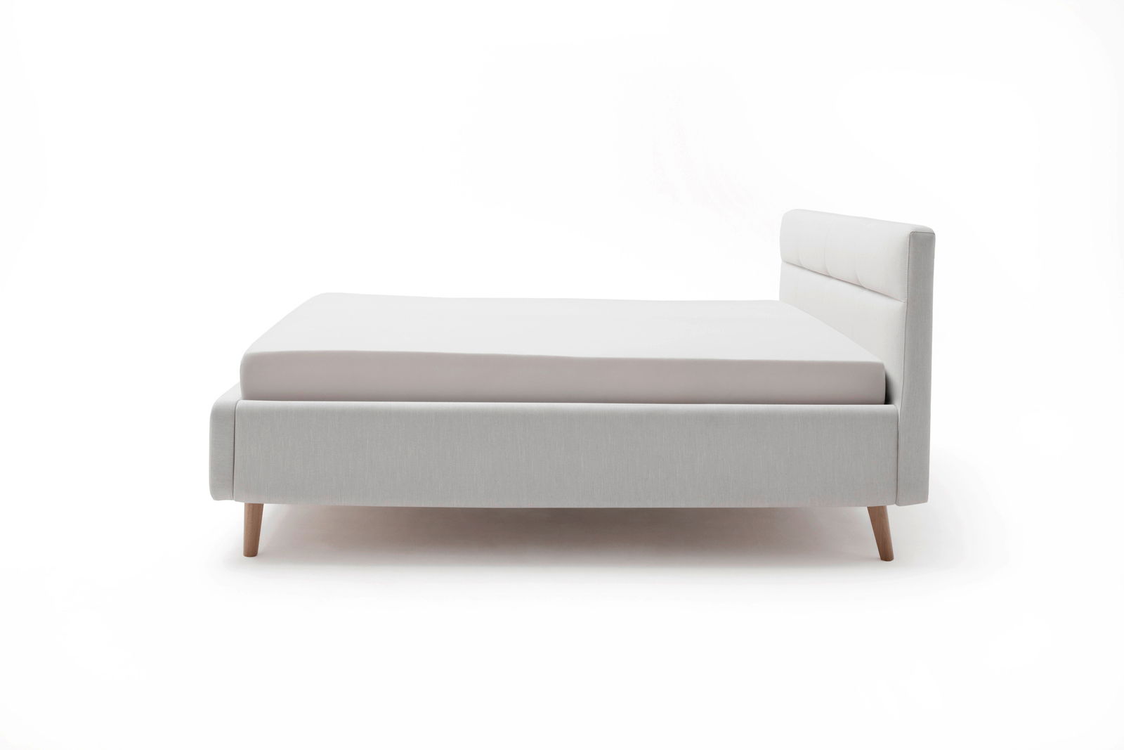 Seitenansicht eines modernen Polsterbetts in hellem Grau mit Holzfüßen und gepolstertem Kopfteil.