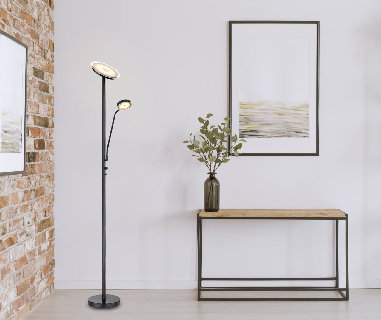 Moderne Stehleuchte mit zwei verstellbaren Leuchten, in einem stilvollen Wohnzimmer mit Ziegelwand und minimalistischem Dekor, seitliche Perspektive.