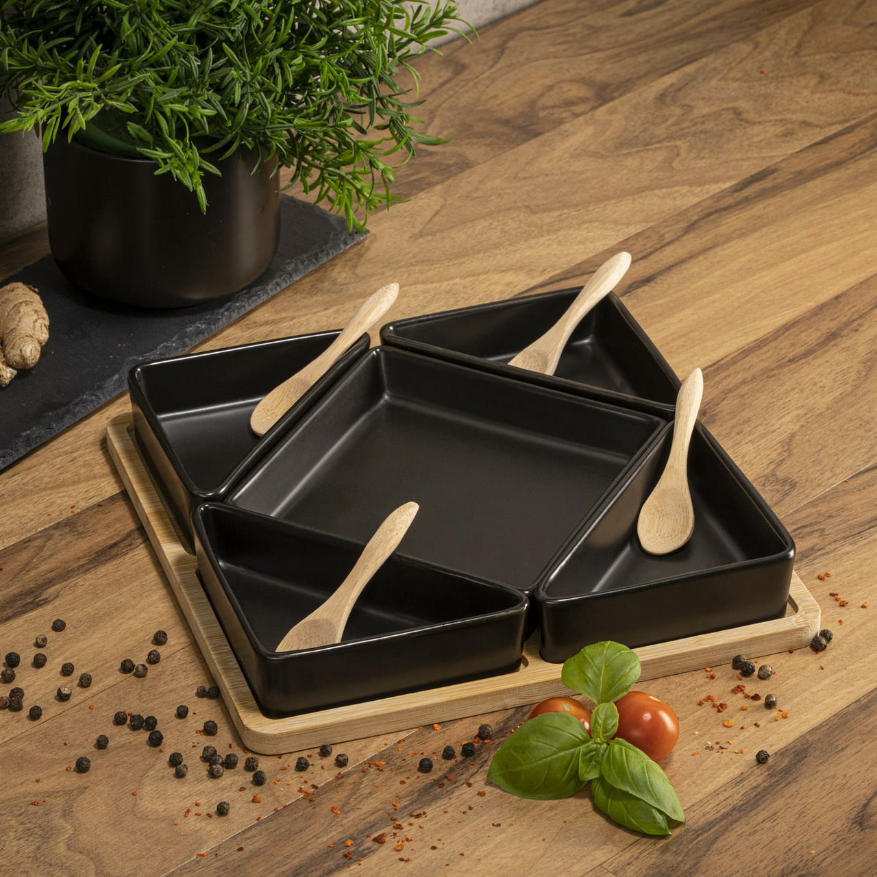 Servierset aus Bambus mit fünf schwarzen Schalen und Holzlöffeln, von oben fotografiert auf einem Holztisch, dekoriert mit Gewürzen und frischen Kräutern.