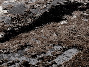 Nahaufnahme eines Designer Teppichs mit abstraktem Muster in Braun-, Grau- und Schwarztönen, aus der Vogelperspektive fotografiert.