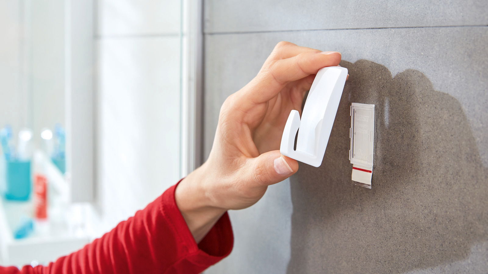 Hand befestigt einen weißen tesa Powerstrip Haken an einer Badezimmerfliese, seitliche Perspektive.