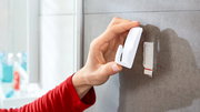 Hand befestigt einen weißen tesa Powerstrip Haken an einer Badezimmerfliese, seitliche Perspektive.