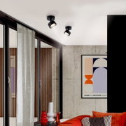 Zwei schwarze, schwenkbare Deckenaufbauspots mit warmweißem Licht in modernem Wohnzimmer, fotografiert aus leicht schräger Untersicht auf die Decke.