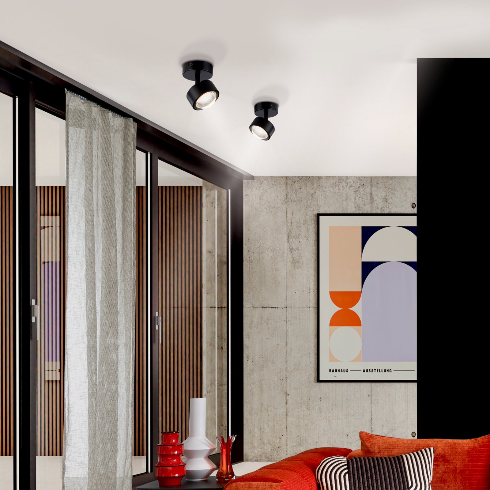 Zwei schwarze, schwenkbare Deckenaufbauspots mit warmweißem Licht in modernem Wohnzimmer, fotografiert aus leicht schräger Untersicht auf die Decke.