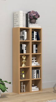 Modernes, schmales Bücherregal aus hellem Holz mit mehreren offenen Fächern, gefüllt mit Büchern und Deko; oben liegen große Bildbände und eine Vase mit violetten Hortensien, fotografiert in frontaler Perspektive leicht von links in einem hellen Wohnraum.