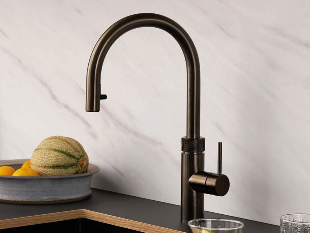 Moderne Küchenarmatur aus dunkler Bronze mit gewölbtem Auslauf, positioniert neben einem Teller mit Früchten.