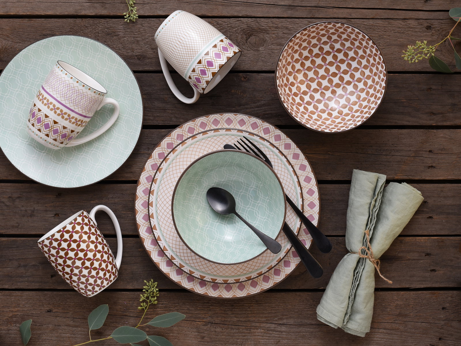 Kombiservice 16-tlg mit bunten Mustern, bestehend aus Tellern, Schalen und Tassen, auf einem Holztisch von oben fotografiert.