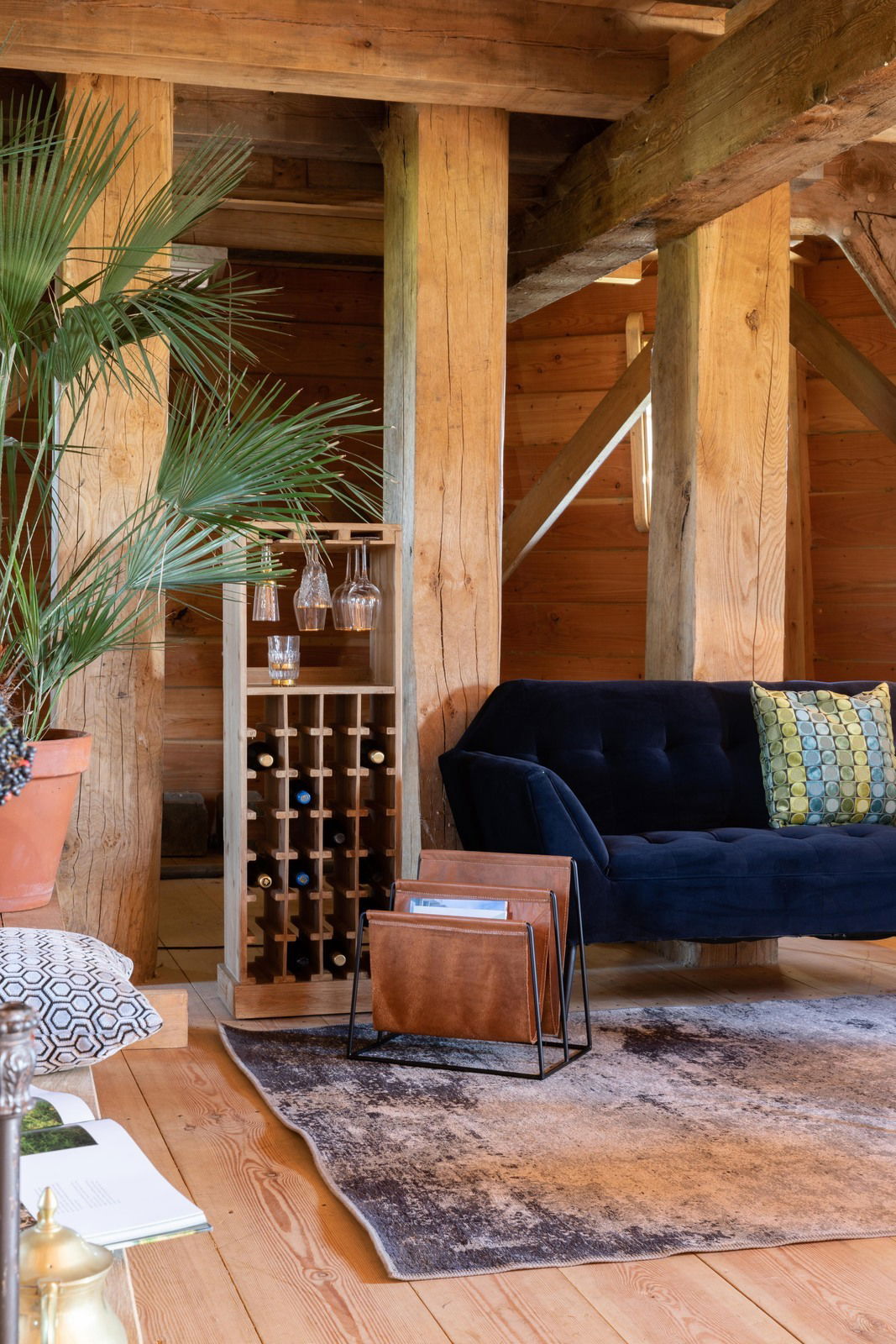 Holz-Weinregal in einem gemütlichen Wohnzimmer mit einem blauen Sofa und Pflanzen, seitliche Perspektive.