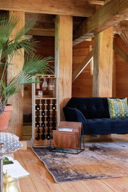 Holz-Weinregal in einem gemütlichen Wohnzimmer mit einem blauen Sofa und Pflanzen, seitliche Perspektive.