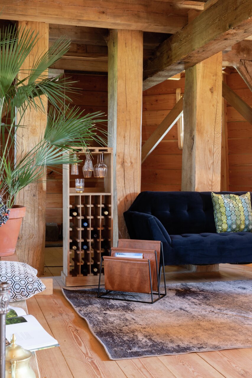 Holz-Weinregal in einem gemütlichen Wohnzimmer mit einem blauen Sofa und Pflanzen, seitliche Perspektive.