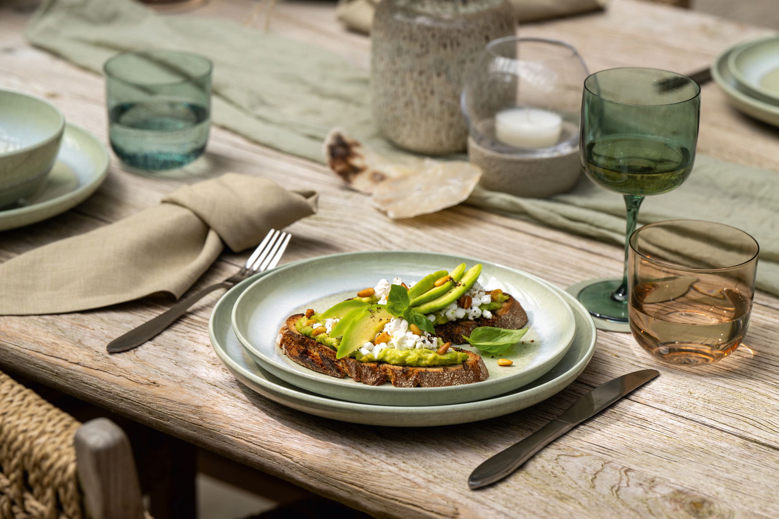 Like by Villeroy & Boch Speiseteller PERLEMOR ALGA Ein gedeckter Tisch mit einem grünen Speiseteller, darauf Avocado-Toast mit Hüttenkäse und Pinienkernen. Perspektive von schräg oben.