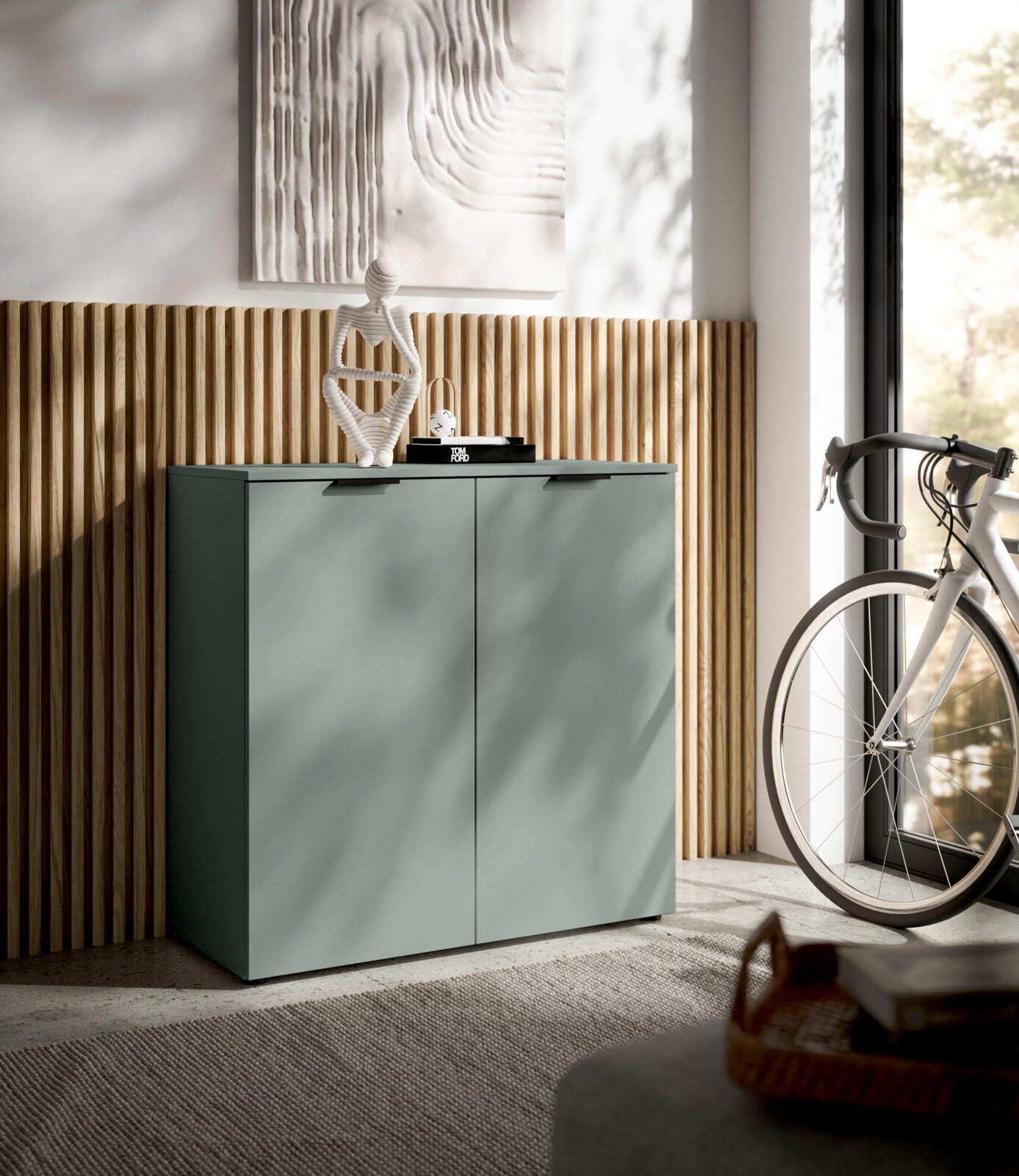 Moderne Kommode in einem hellen Raum, seitliche Perspektive, mit Dekoration und Fahrrad im Hintergrund.