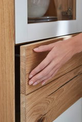 Nahaufnahme einer Hand, die eine Holzschublade eines Stauraumelements öffnet. Die Perspektive zeigt die Schublade von der Seite.