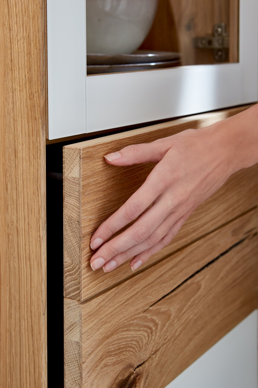 Nahaufnahme einer Hand, die eine Holzschublade eines Stauraumelements öffnet. Die Perspektive zeigt die Schublade von der Seite.