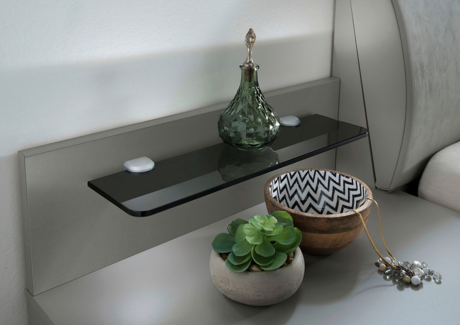Nachtkonsolen Paneel mit Glasablage, dekoriert mit einer grünen Glasflasche, einer Schale mit Zickzackmuster und einem kleinen Pflanzentopf, seitliche Perspektive