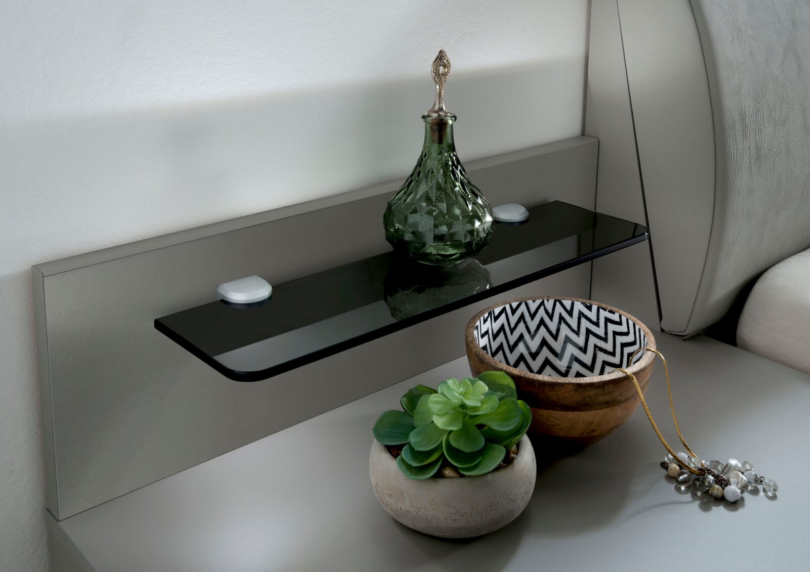 Venda Nachtkonsolen Paneel VIGO Nachtkonsolen Paneel mit Glasablage, dekoriert mit einer grünen Glasflasche, einer Schale mit Zickzackmuster und einem kleinen Pflanzentopf, seitliche Perspektive