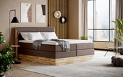 Een modern boxspringbed in een stijlvolle slaapkamer, gezien vanaf de zijkant, met grote ramen en een elegante inrichting.