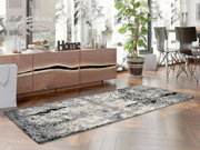 Moderner Designer Teppich in Grau- und Beigetönen auf einem Holzboden, umgeben von stilvollen Möbeln und Pflanzen, aus seitlicher Perspektive fotografiert.