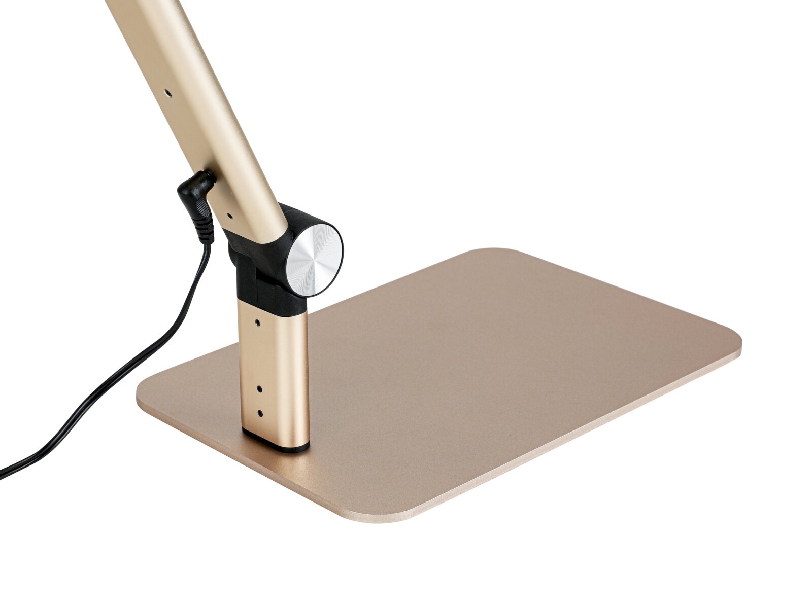Nahaufnahme des Sockels einer goldfarbenen Schreibtischlampe mit rechteckiger Standplatte, Drehgelenk und angeschlossenem Stromkabel, schräg von der Seite aufgenommen.