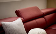 Nahaufnahme eines roten Ledersofas mit verstellbarer Kopfstütze und weißen Kissen, seitliche Perspektive