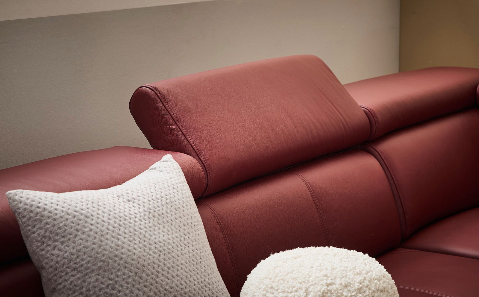Nahaufnahme eines roten Ledersofas mit verstellbarer Kopfstütze und weißen Kissen, seitliche Perspektive