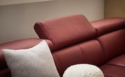 Nahaufnahme eines roten Ledersofas mit verstellbarer Kopfstütze und weißen Kissen, seitliche Perspektive
