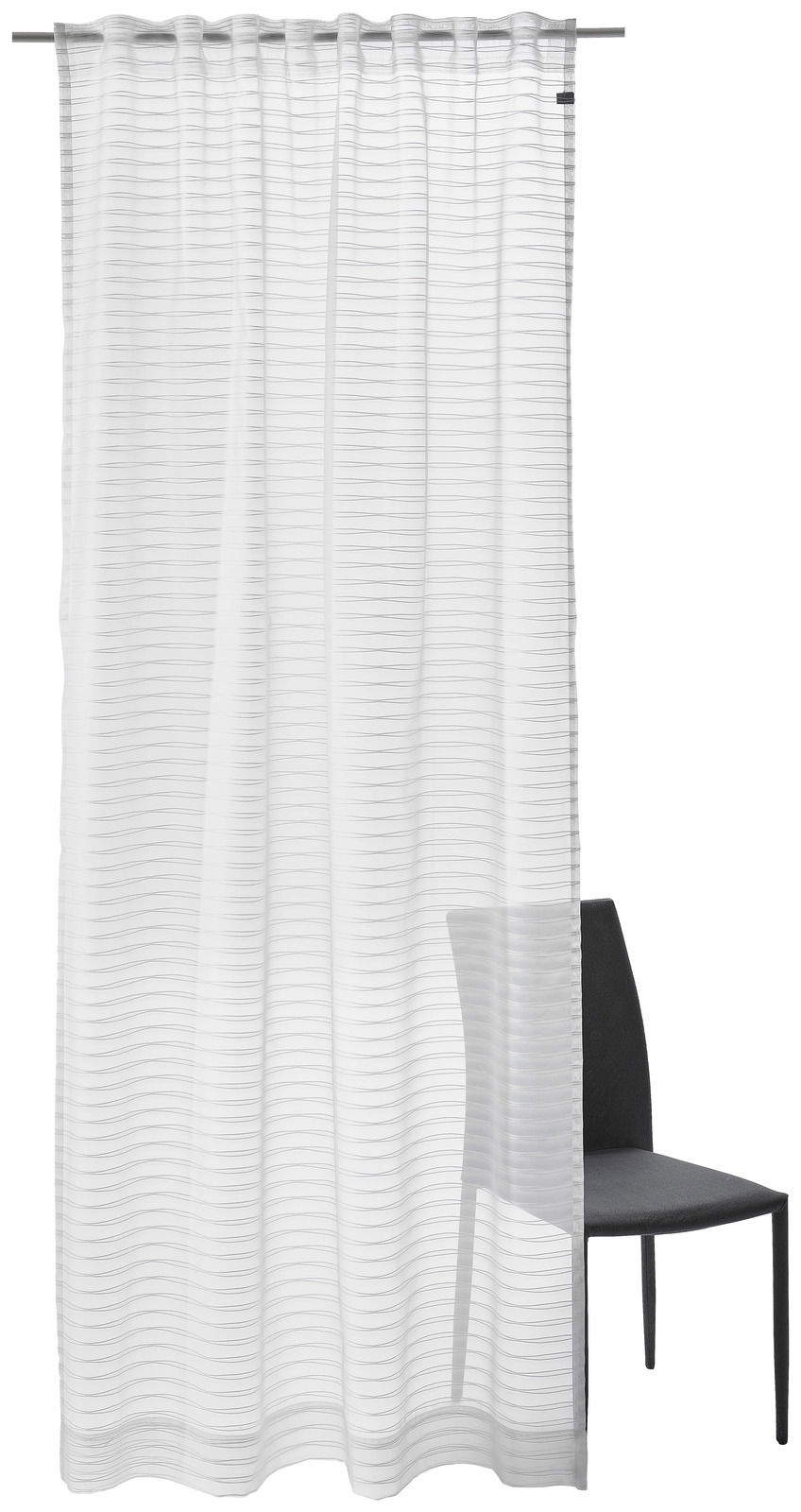 Weißer Dekoschal mit feinen horizontalen Linien, aufgehängt an einer Gardinenstange, mit einem Stuhl im Hintergrund. Frontalansicht.
