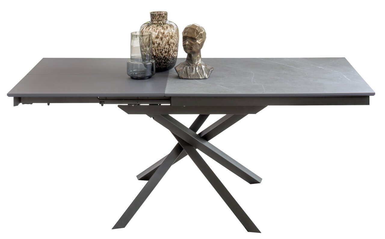 Moderner Esstisch mit grauer Tischplatte und gekreuztem Metallgestell, seitliche Perspektive, dekoriert mit Vasen und einer Skulptur.