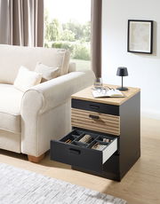 Rollcontainer mit offenem Schubfach, gefüllt mit Accessoires, neben einem Sofa in einem Wohnzimmer, aus seitlicher Perspektive fotografiert.