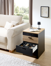 Rollcontainer mit offenem Schubfach, gefüllt mit Accessoires, neben einem Sofa in einem Wohnzimmer, aus seitlicher Perspektive fotografiert.