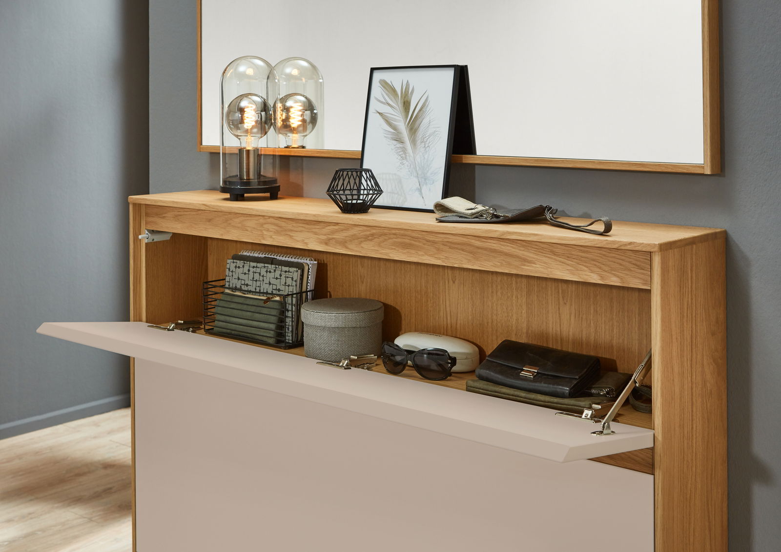 VOSS Schuhschrank V100 Moderner Schuhschrank aus Holz mit offener Klappe, dekoriert mit Lampen und Bildern, aus der Frontalperspektive.