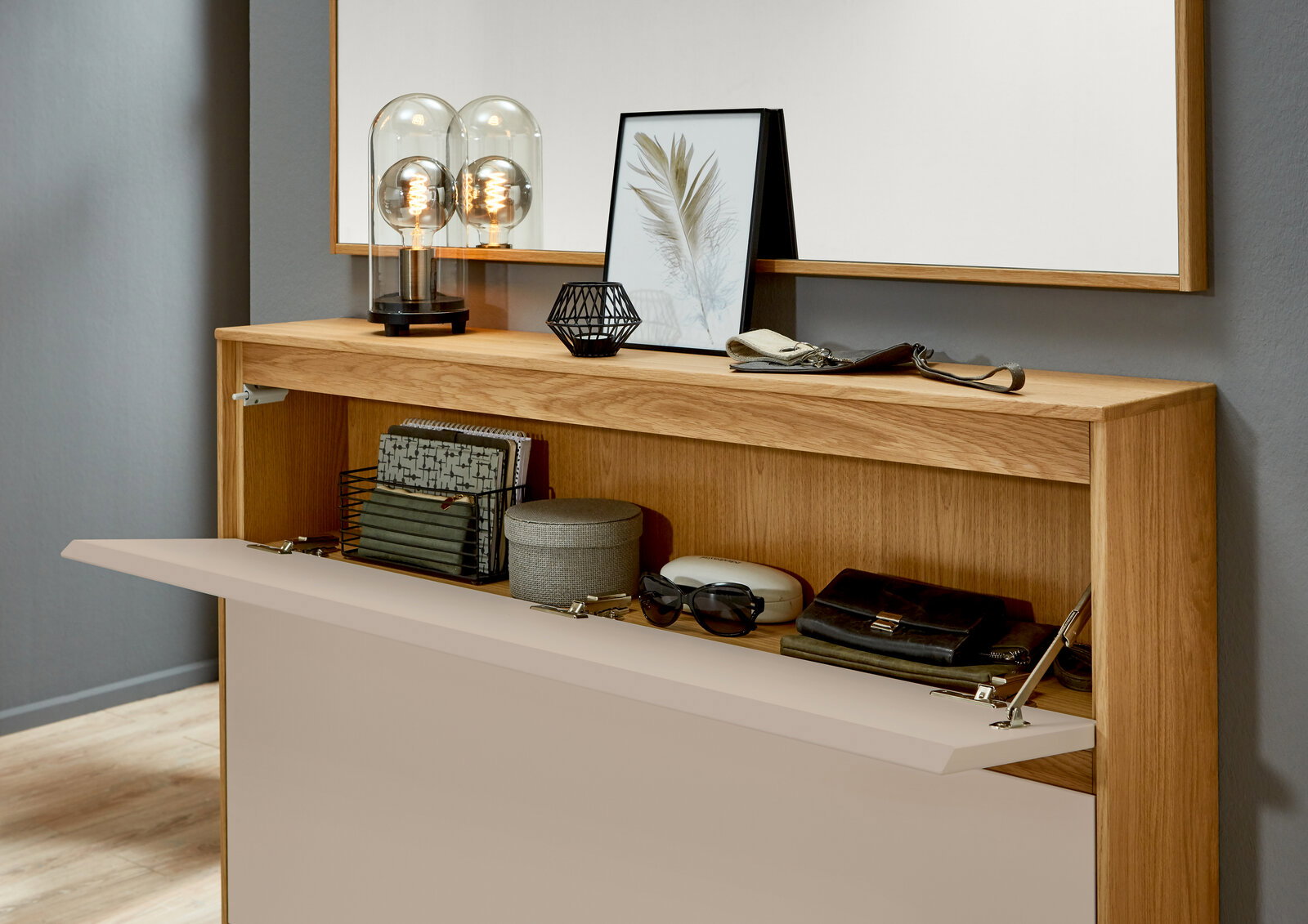 VOSS Schuhschrank V100 Moderner Schuhschrank aus Holz mit offener Klappe, dekoriert mit Lampen und Bildern, aus der Frontalperspektive.