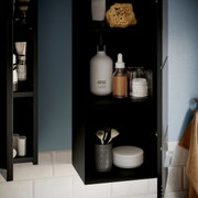 Schwarzer Badezimmerschrank mit offenen Regalen, gefüllt mit Pflegeprodukten und Accessoires, aus seitlicher Perspektive.