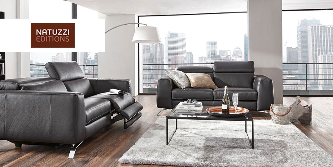 Ein Wohnzimmer mit schwarzen Ledersofas, einem Couchtisch aus Glas und dem Natuzzi Editions Logo