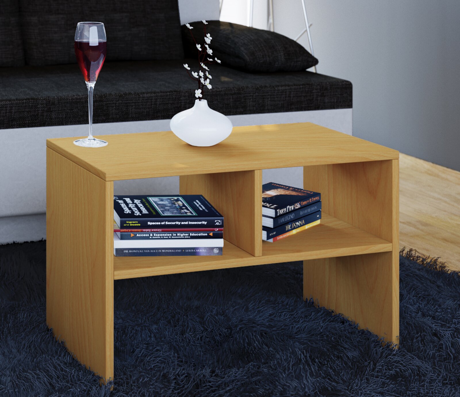 Rechteckiger Couchtisch aus hellem Holz mit zwei offenen Ablagefächern, darauf ein Weinglas und eine weiße Vase, seitliche Perspektive im Wohnzimmer vor grauem Sofa auf blauem Teppich